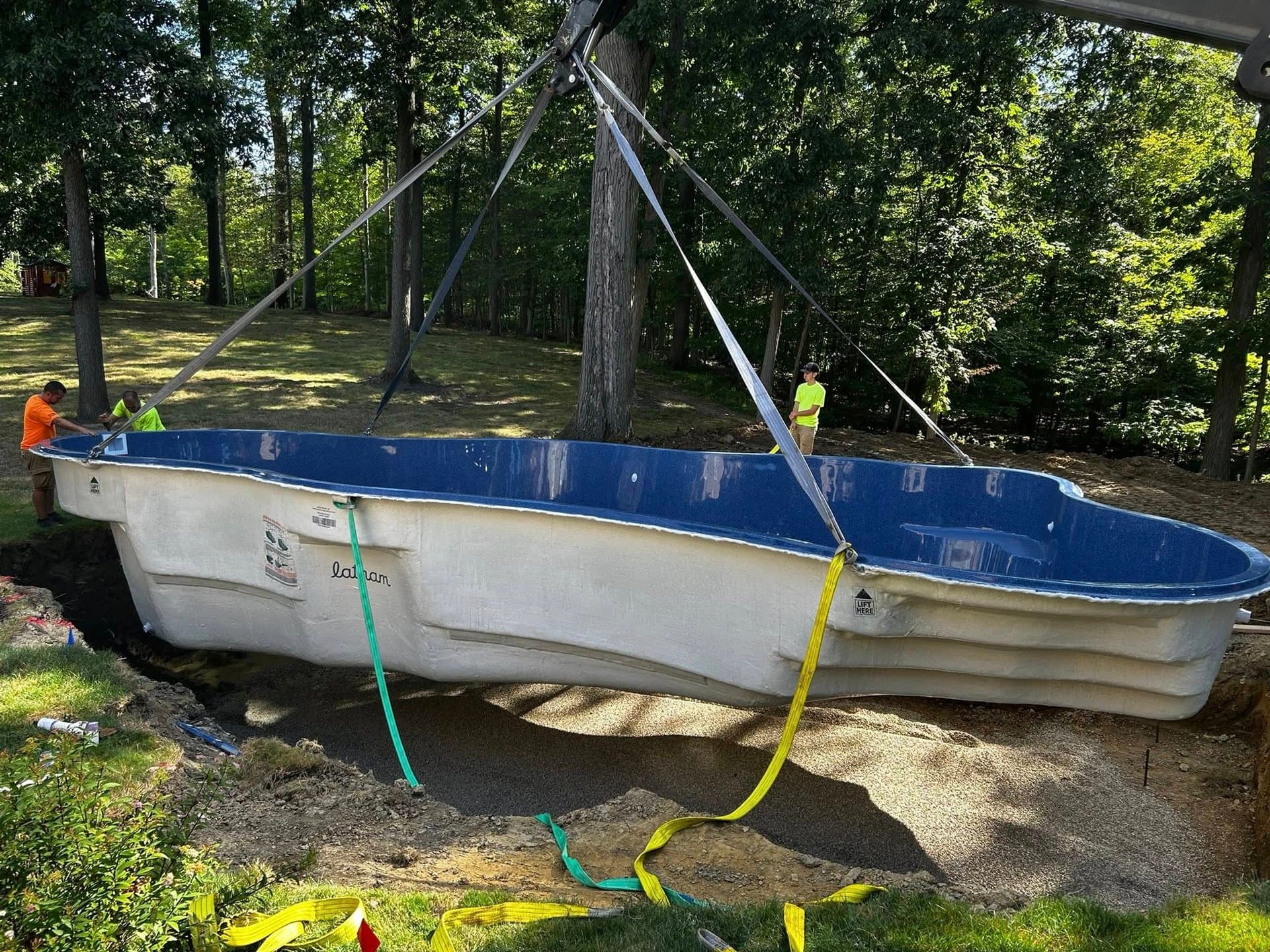 Mini excavator beside a fiberglass pool shell on a wooded lot during an Ohio pool install