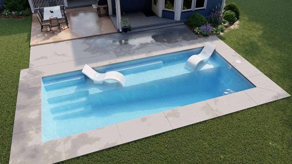 Liberty Anthem fiberglass pool, rectangular pool with a full-length tanning ledge holding two in-water loungers, set in a light concrete deck on a lawn, manufacturer photo.