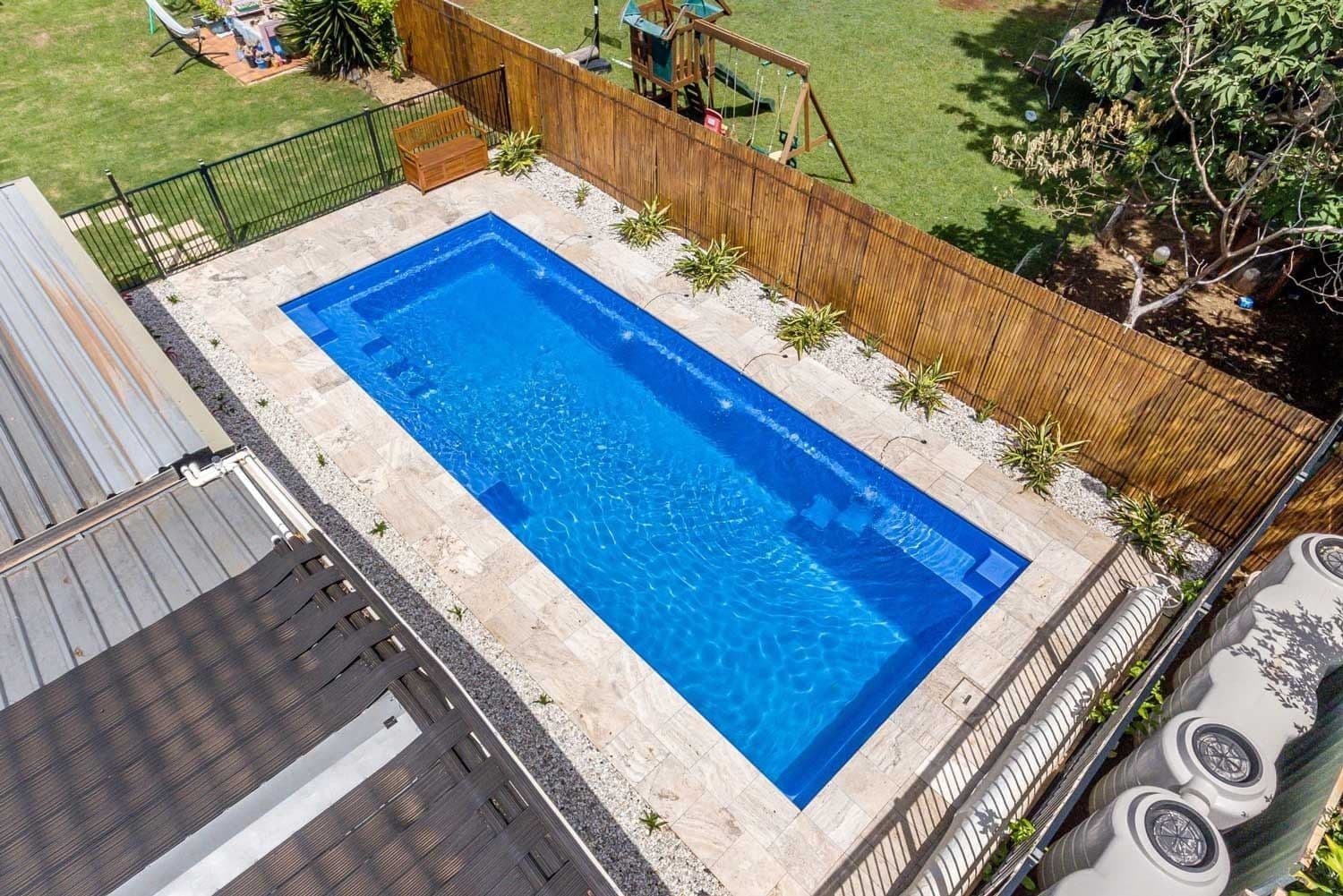 Liberty Compassion fiberglass pool, overhead view of a small rectangular pool with a stone deck beside a wooden privacy fence, manufacturer photo.