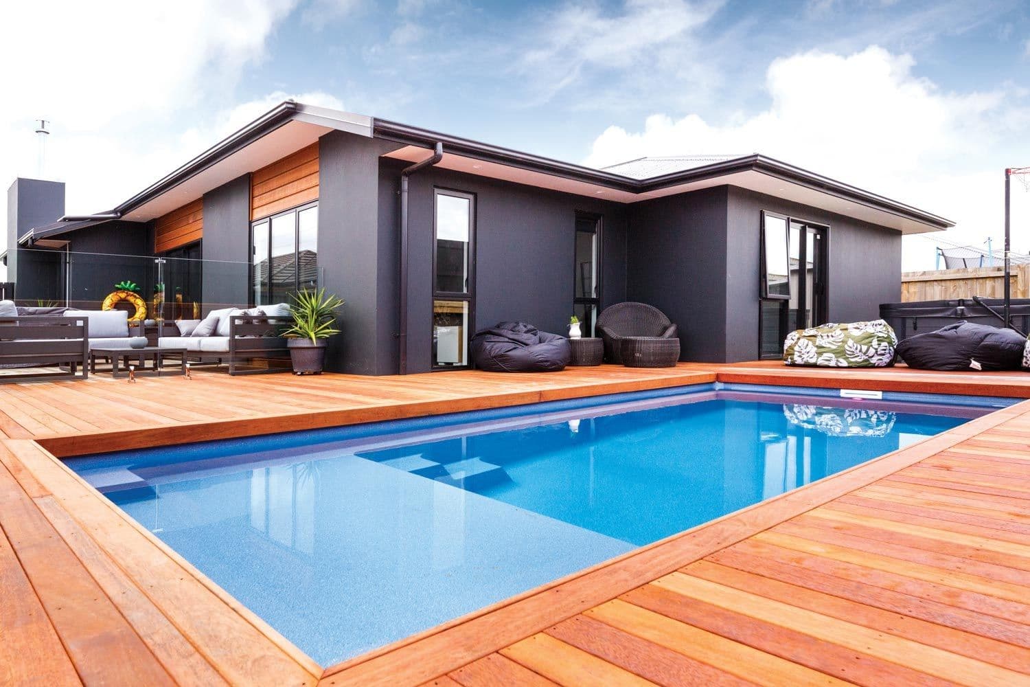Liberty Enrichment fiberglass pool, small rectangular pool with entry steps set in a red wood deck beside a modern dark-clad house, manufacturer photo.