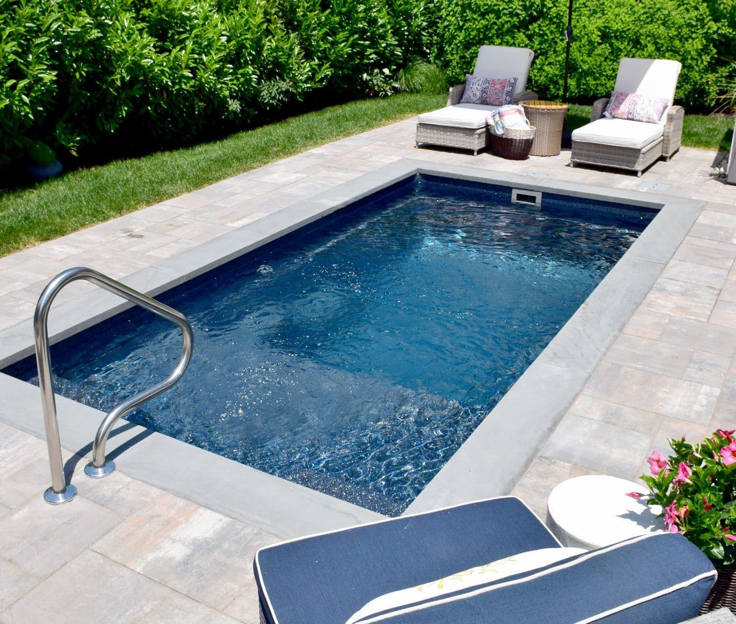 Liberty Enrichment fiberglass pool, small rectangular pool with a dark interior and a handrail, gray stone coping and two lounge chairs, manufacturer photo.