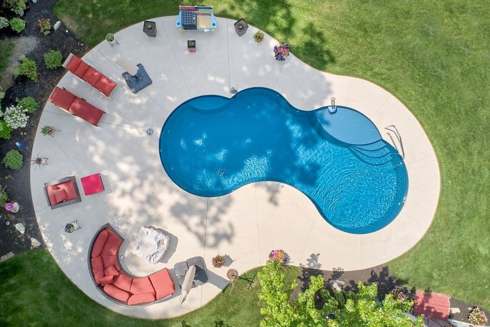 Liberty Finesse fiberglass pool, aerial view of a figure-eight pool with a round concrete deck, red lounge chairs and a lawn, manufacturer photo.
