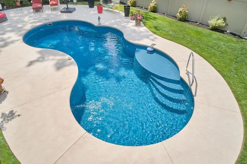 Liberty Finesse fiberglass pool, figure-eight pool with corner entry steps and a handrail on a wide light concrete deck, manufacturer photo.