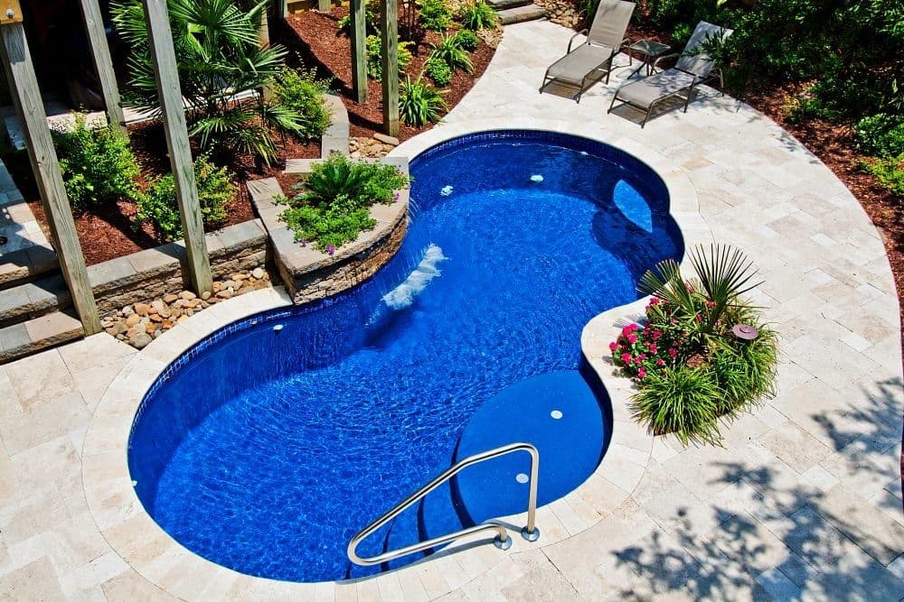 Liberty Finesse fiberglass pool, figure-eight pool with a dark blue interior, travertine deck and a planted border seen from above, manufacturer photo.