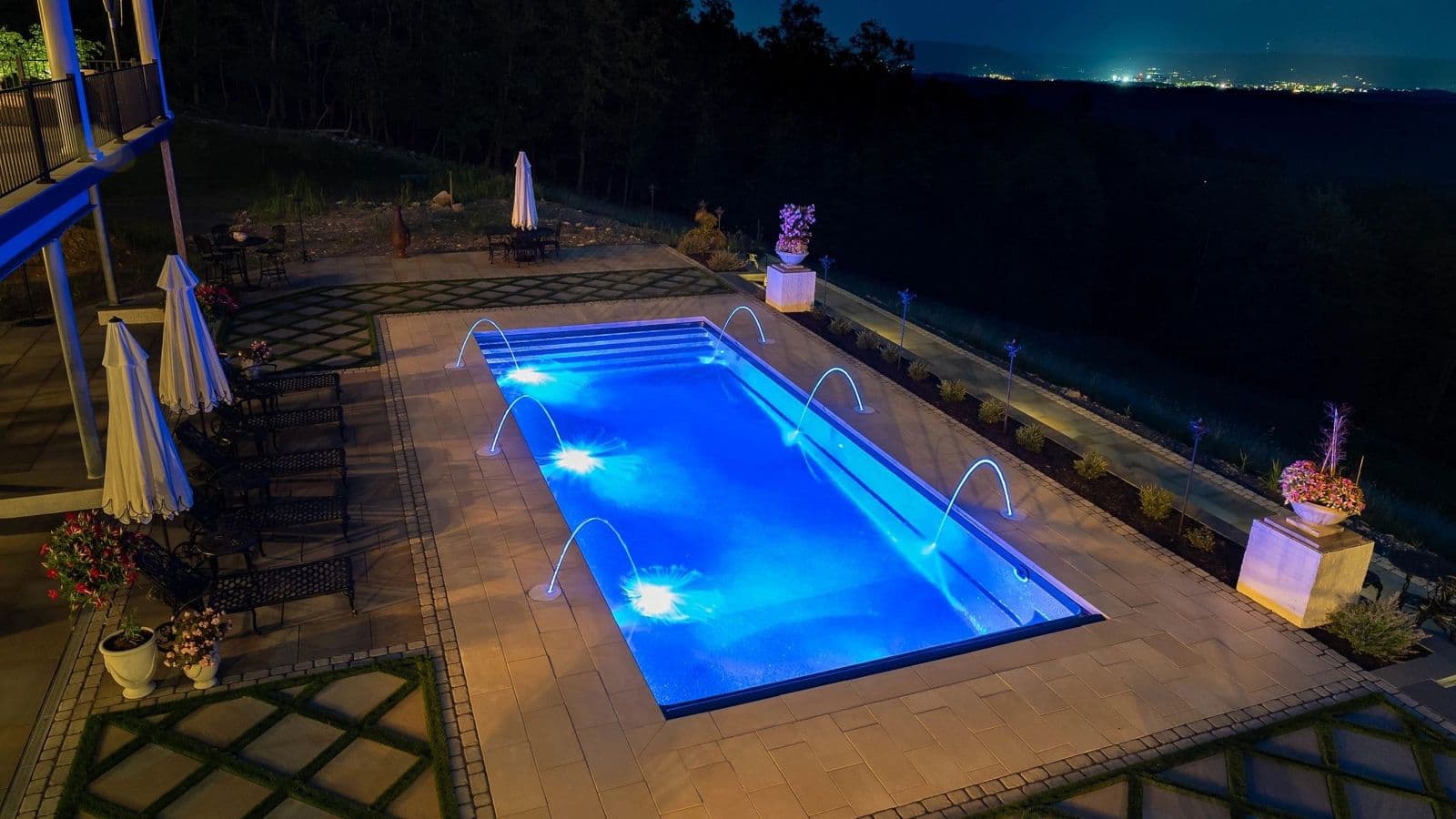 Liberty Glory fiberglass pool, rectangular pool lit blue at night on a stone patio, manufacturer photo.