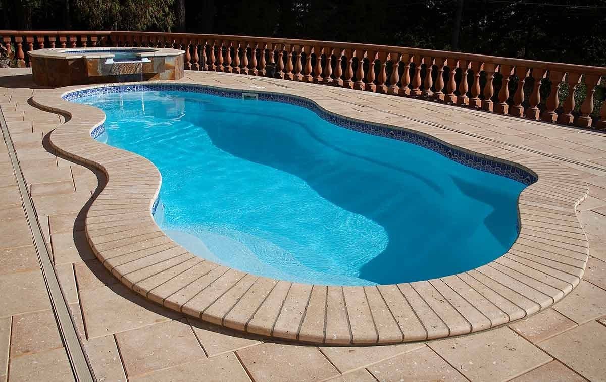 Liberty Hero fiberglass pool, freeform pool with a light blue interior, a brick paver deck and a stone balustrade, manufacturer photo.
