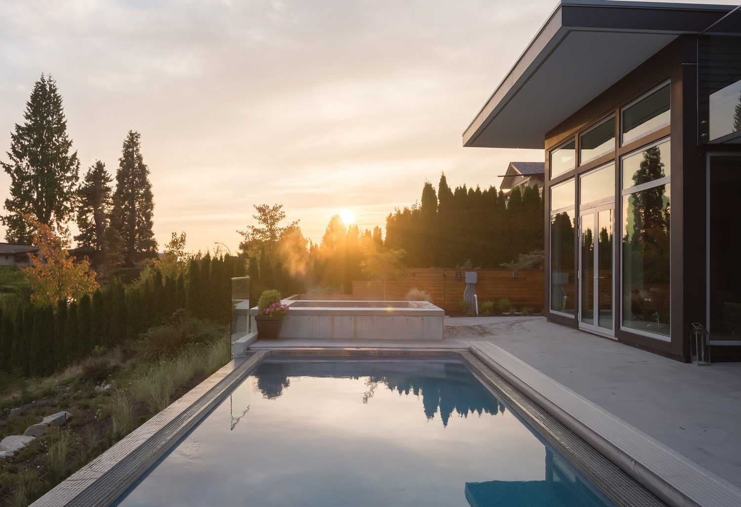 Liberty Independence fiberglass pool, rectangular pool with a raised spa at the far end, reflecting a sunset beside a modern house, manufacturer photo.