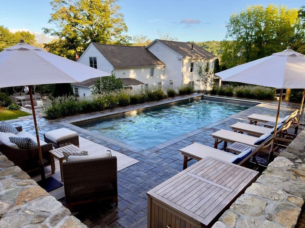 Liberty Opportunity fiberglass pool, rectangular pool with tile trim, lounge chairs, umbrellas and a flagstone patio in a garden, manufacturer photo.