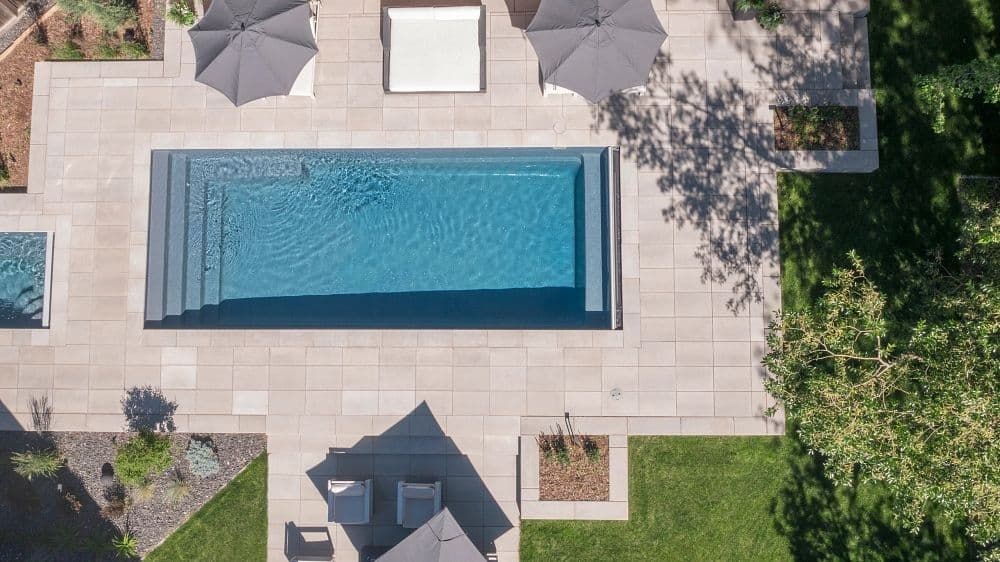 Liberty Opportunity fiberglass pool, aerial view of a rectangular pool with a light stone deck, umbrellas and lawn, manufacturer photo.