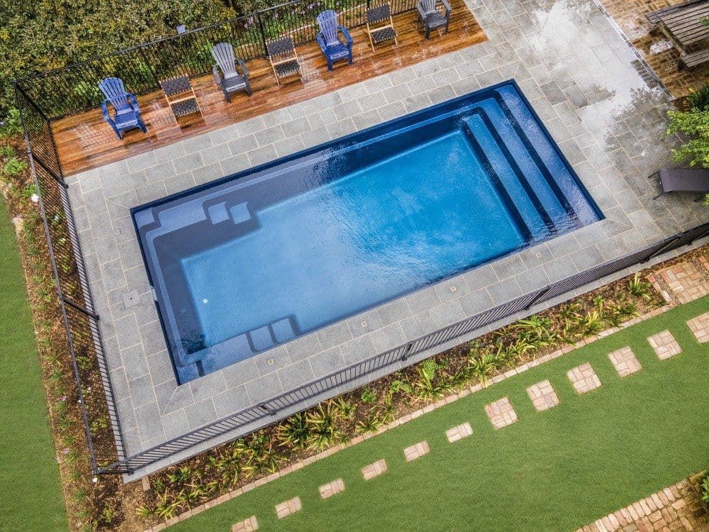 Liberty Stature fiberglass pool, aerial view of a rectangular pool with stepped entry, a light stone deck, lounge chairs and a stepping-stone path, manufacturer photo.