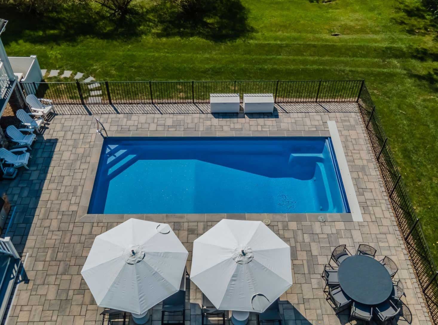 Liberty Valiant fiberglass pool, aerial view of a rectangular pool with entry steps, gray pavers, white umbrellas and dining set, manufacturer photo.