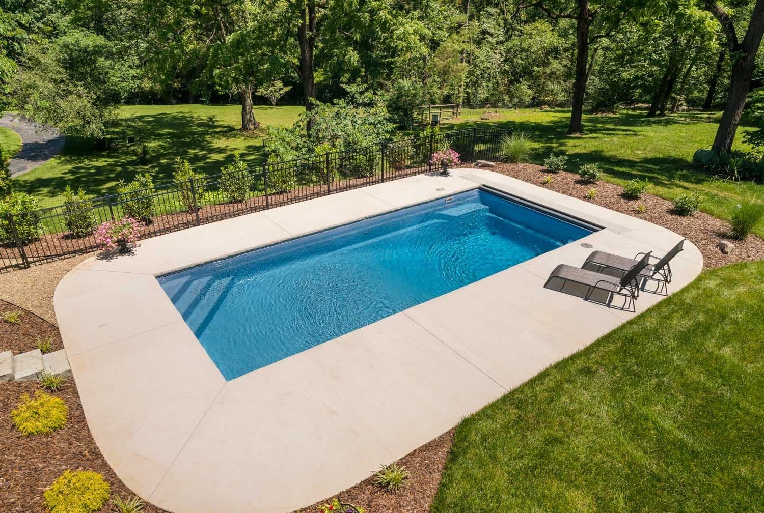 Liberty Valiant fiberglass pool, rectangular pool with a light concrete deck and lounge chairs set in a lawn with trees behind, manufacturer photo.