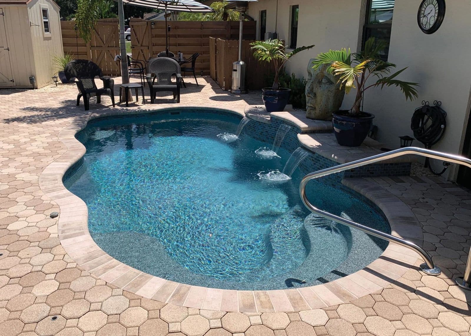 Liberty Victory fiberglass pool, freeform pool with a gray interior and an octagon paver deck, with a handrail and patio furniture, manufacturer photo.
