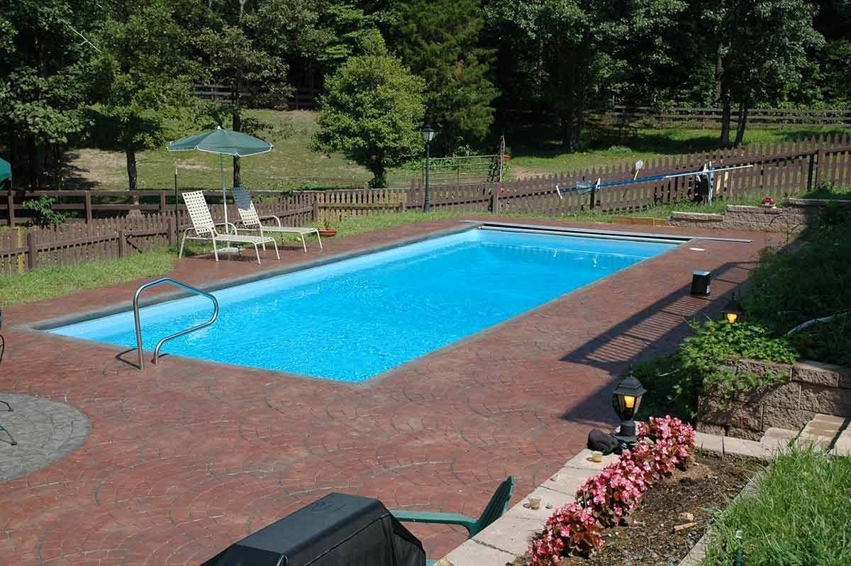 Liberty Virtuous fiberglass pool, long rectangular pool with a light blue interior and a red brick deck along a fence, manufacturer photo.